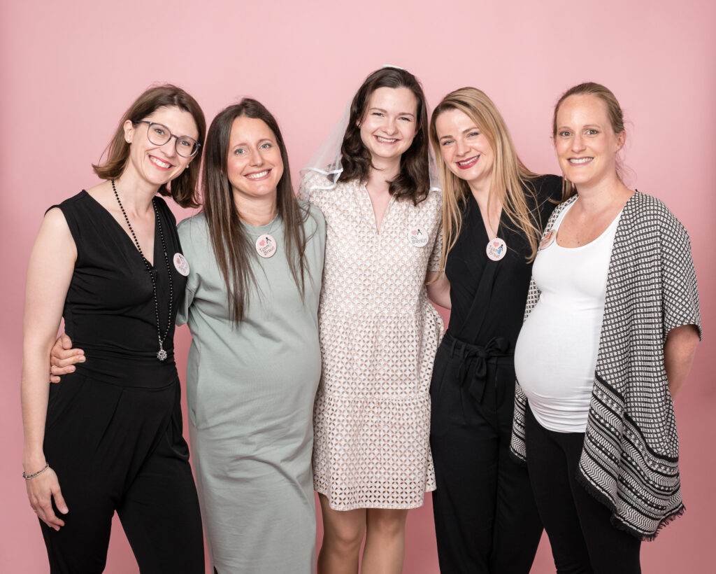 Gruppe fröhlicher Frauen bei einer Bridal Shower – Braut mit Freundinnen vor rosa Hintergrund